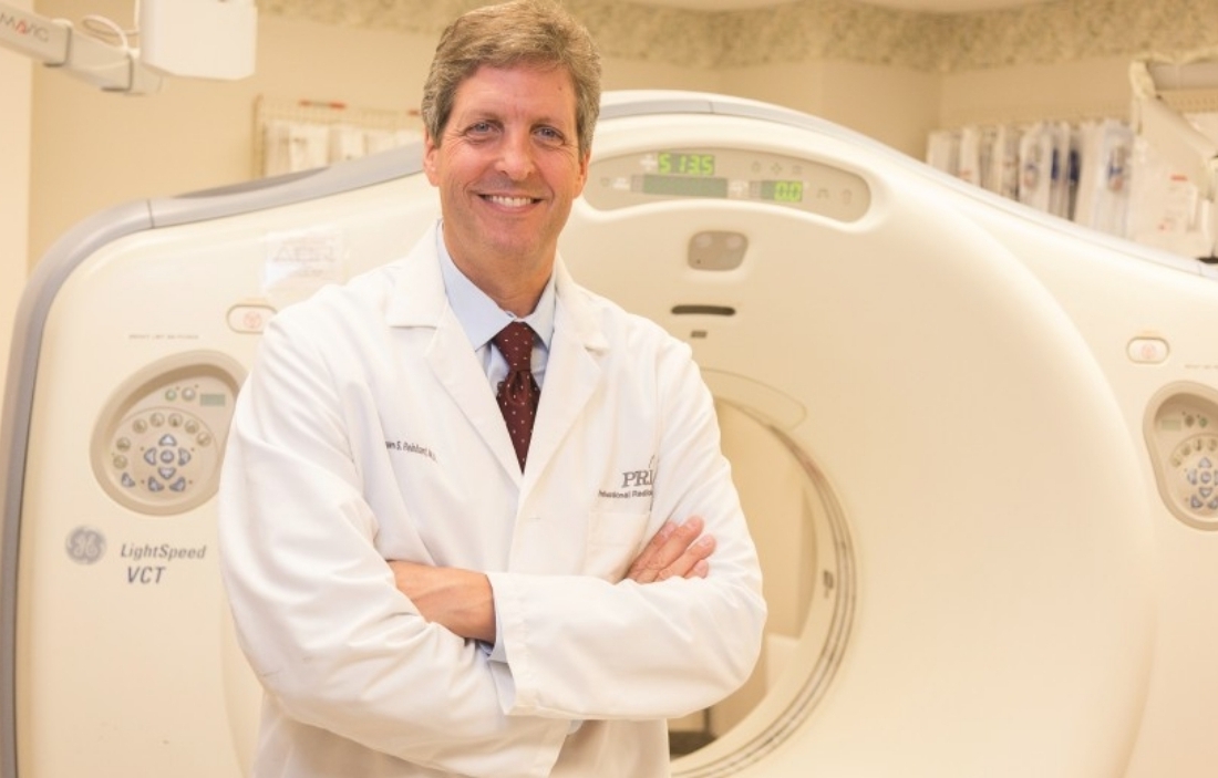 male doctor with arms crossed in front of machine